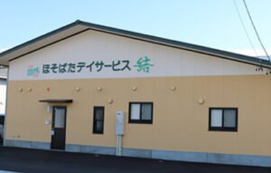 居宅介護サービス事業所の建物外観。ベージュ色の平屋建て施設。