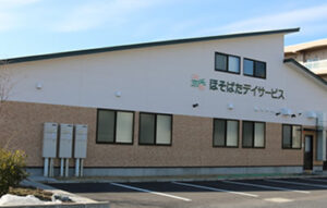 介護施設の建物外観。ベージュ色の外壁と茶色レンガ貼りの低層建物。